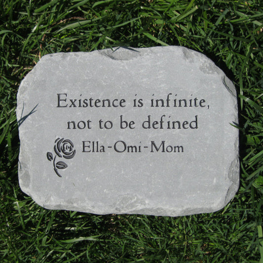 A custom engraved stone memorial plaque lying on green grass, featuring the quote 'Existence is infinite, not to be defined' and the name 'Ella-Omi-Mom' alongside a small rose engraving.