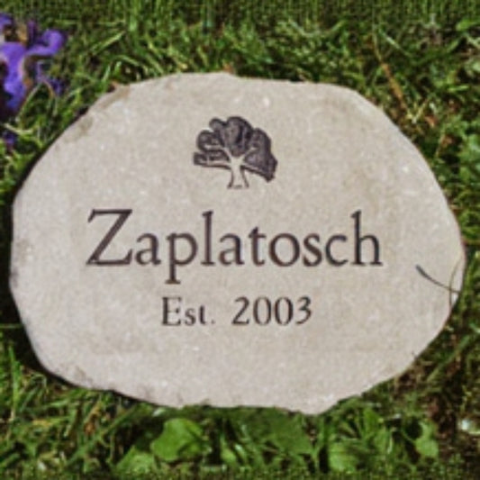 A personalized brown stone marker with a name and, 'Est. 2003', and a tree engraving, placed on green grass with purple flowers in the corner.