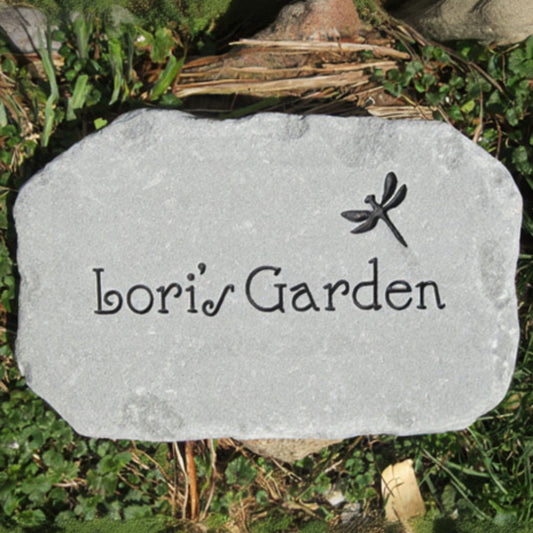 A custom engraved garden stone with the text 'Bori's Garden' and a dragonfly design, placed on grass and soil.