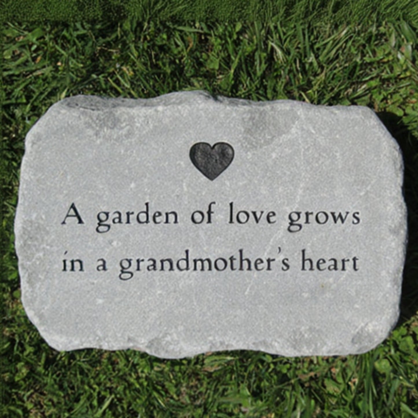 A rectangular garden stone with engraved text reading 'A garden of love grows in a grandmother's heart' and a small heart emblem, placed on green grass.