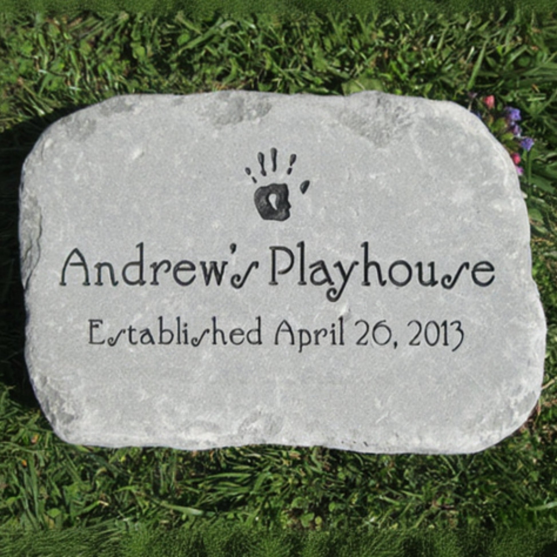 A personalized light gray stone plaque engraved with a handprint icon, the text 'Andrew's Playhouse', and 'Established April 26, 2013', placed on green grass.