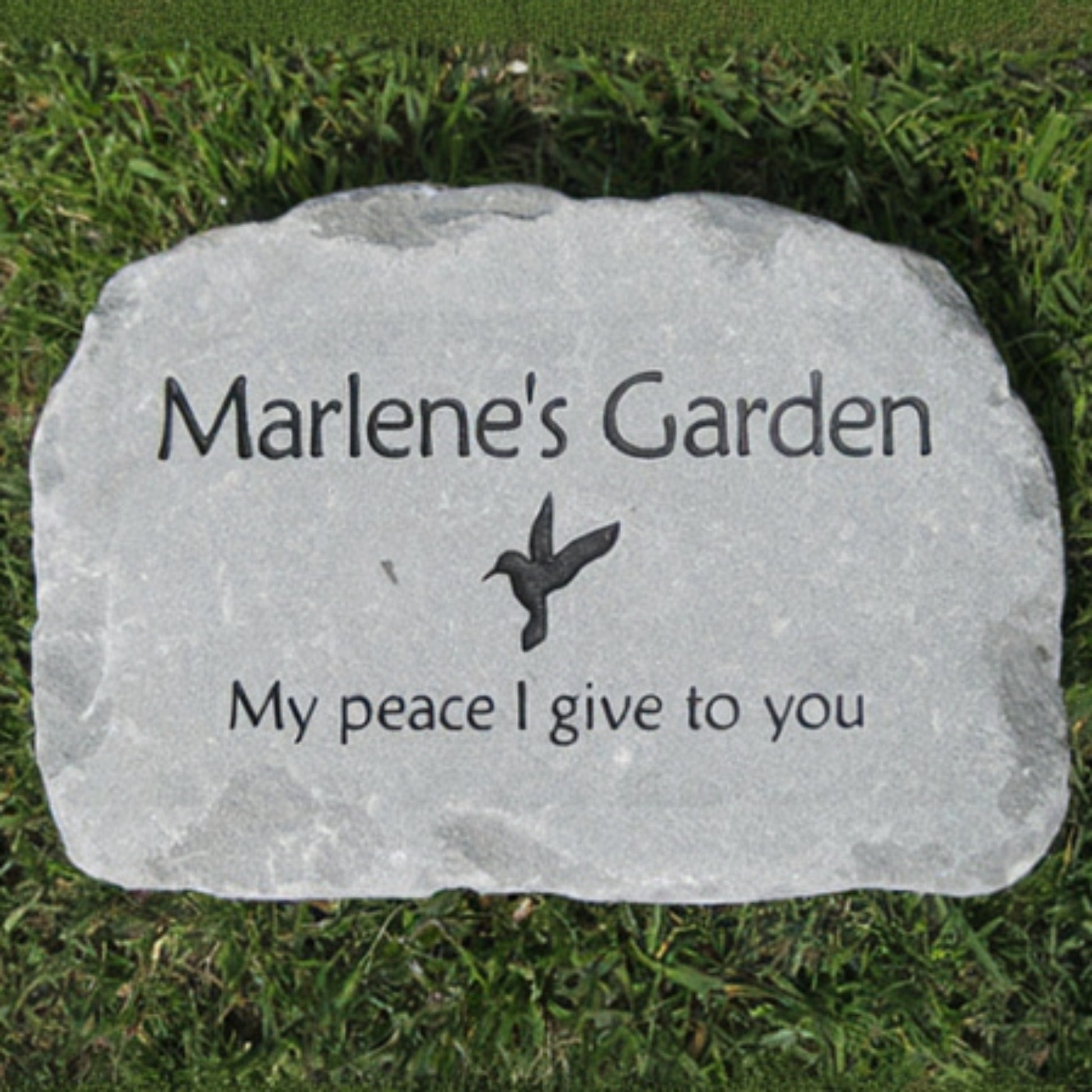 A personalized garden stone marker engraved with 'Marlene's Garden', a small bird silhouette, and 'My peace I give to you', placed on green grass.