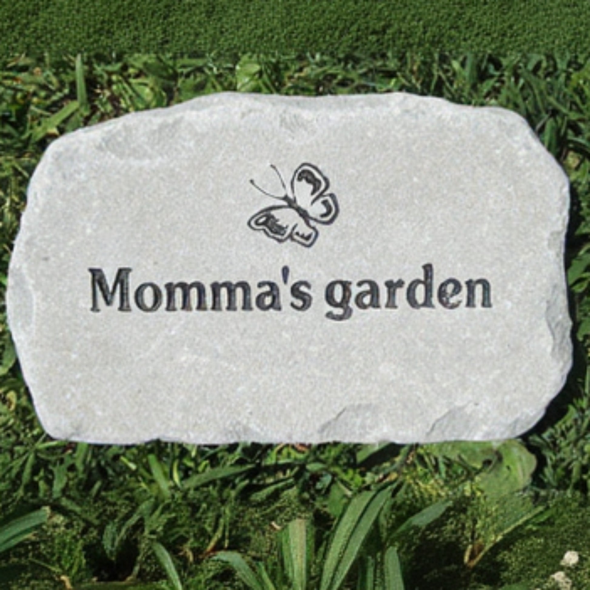 A light gray natural stone garden marker engraved with a butterfly and the words 'Momma's garden', placed on green grass.