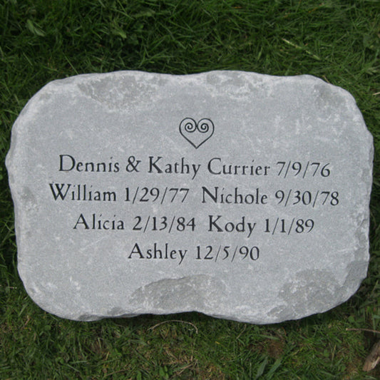 A personalized gray stone  marker with engraved names and dates, placed on green grass. The stone features a small heart design at the top and is inscribed with the text: 'Dennis & Kathy Currier 7/9/76', 'William 1/29/77 Nichole 9/30/78', 'Alicia 2/13/84 Kody 1/1/89', and 'Ashley 12/5/90'.