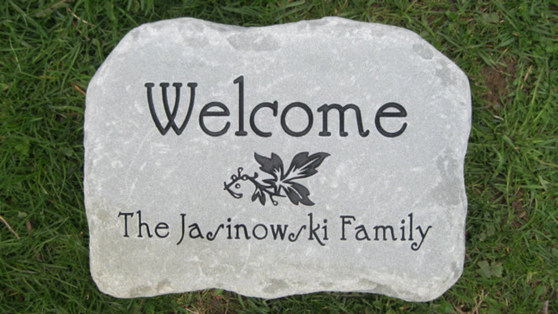 A custom engraved bluestone plaque placed on green grass, featuring the text 'Welcome' and 'The Jasinowki Family' with a small leaf design.