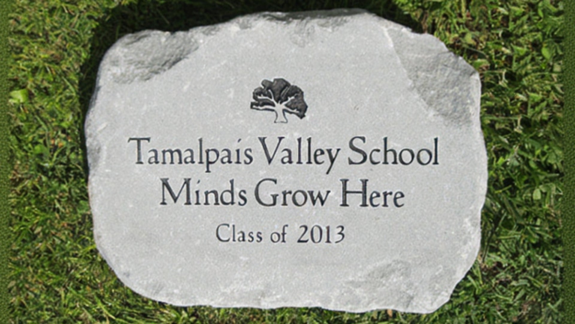 A custom engraved light gray stone outdoor plaque placed on green grass, featuring the text 'Tamalpaís Valley School Minds Grow Here Class of 2013' with a small tree logo at the top.