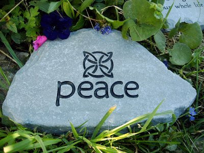 Garden stone that says peace surrounded by flowers and a Celtic knot