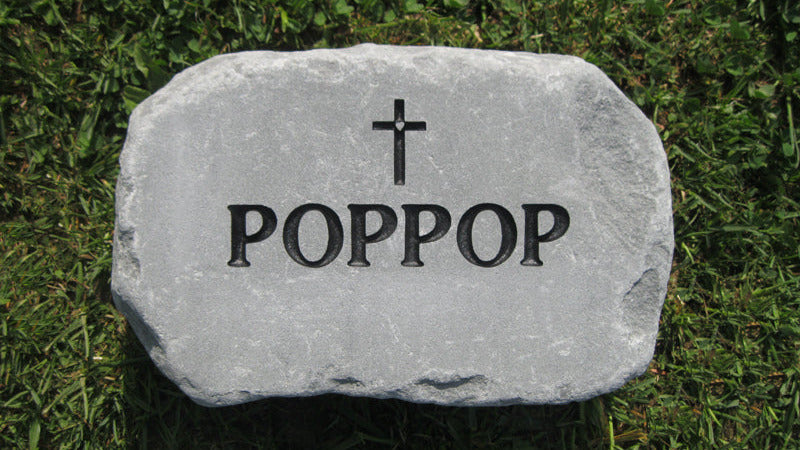 A natural stone  with a black cross and the name 'POPPOP' engraved, placed on green grass.
