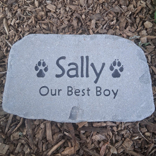 A custom pet memorial garden stone engraved with the name 'Sally', 'Our Best Boy', and paw prints, placed on a bed of brown wood mulch.