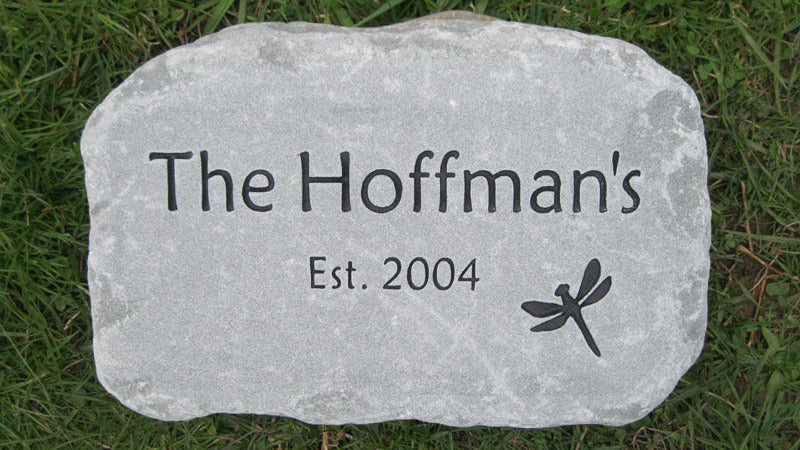 A custom engraved light gray stone plaque with the text 'The Hoffman's Est. 2004' and a dragonfly design, placed on a green grass lawn.