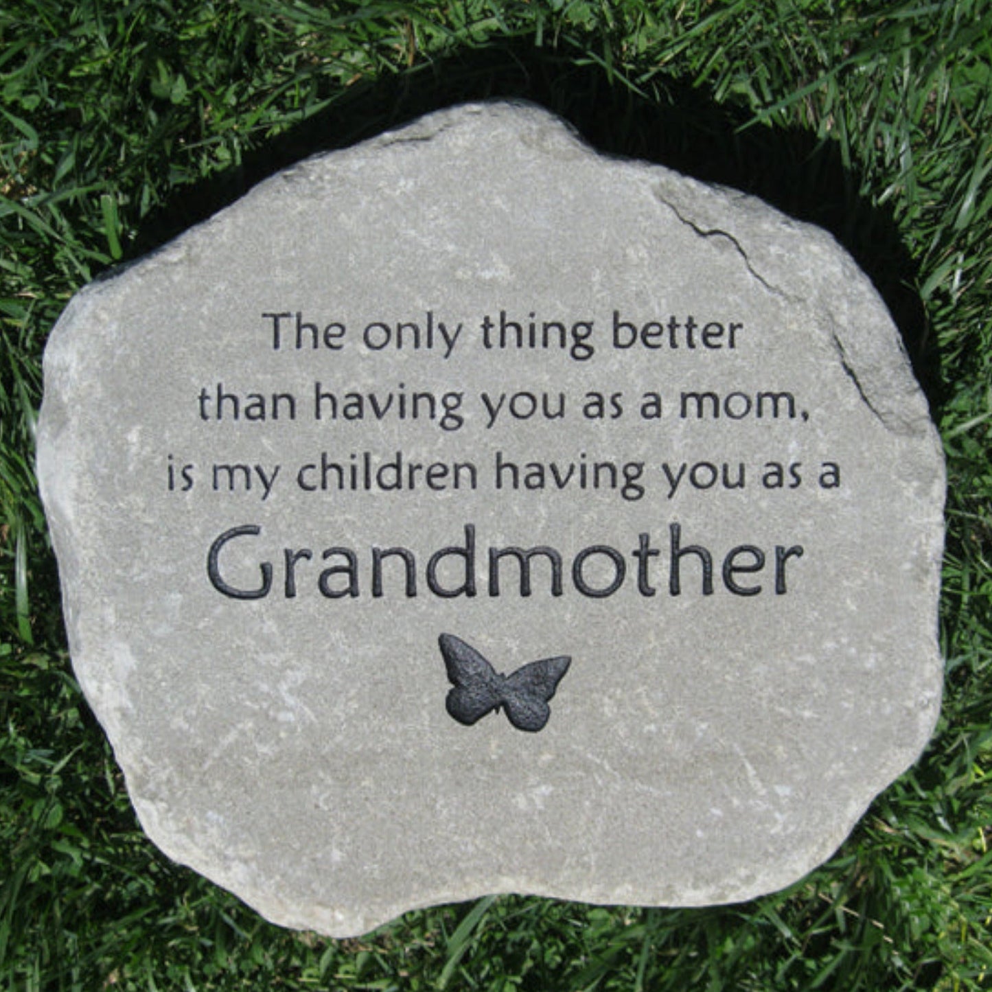 A round natural stone plaque engraved with the phrase 'The only thing better than having you as a mom, is my children having you as a Grandmother' and a small butterfly design, placed on green grass.
