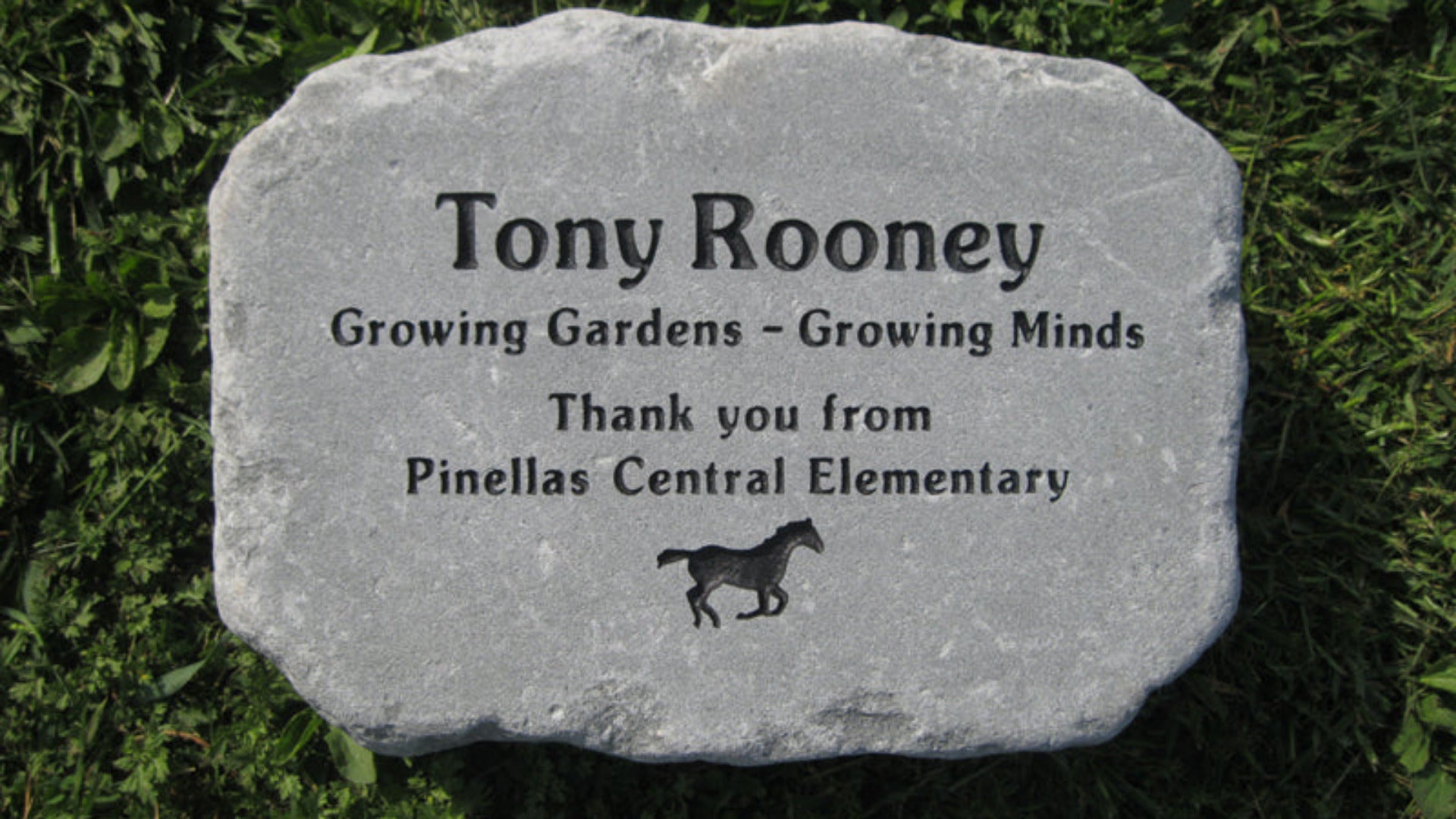 A personalized garden stone  with the name 'Tony Rooney' and a small running horse silhouette, placed on green grass. The plaque includes the text 'Growing Gardens - Growing Minds' and 'Thank you from Pinellas Central Elementary'.